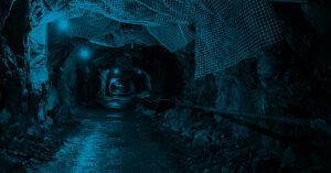 A dark tunnel with a light shining down on it. The tunnel is lined with rocks and has a wire running down the middle.