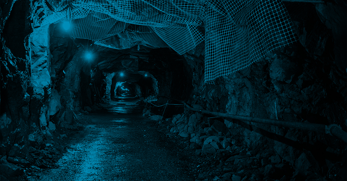 A dark tunnel with a light shining down on it. The tunnel is lined with rocks and has a wire running down the middle.