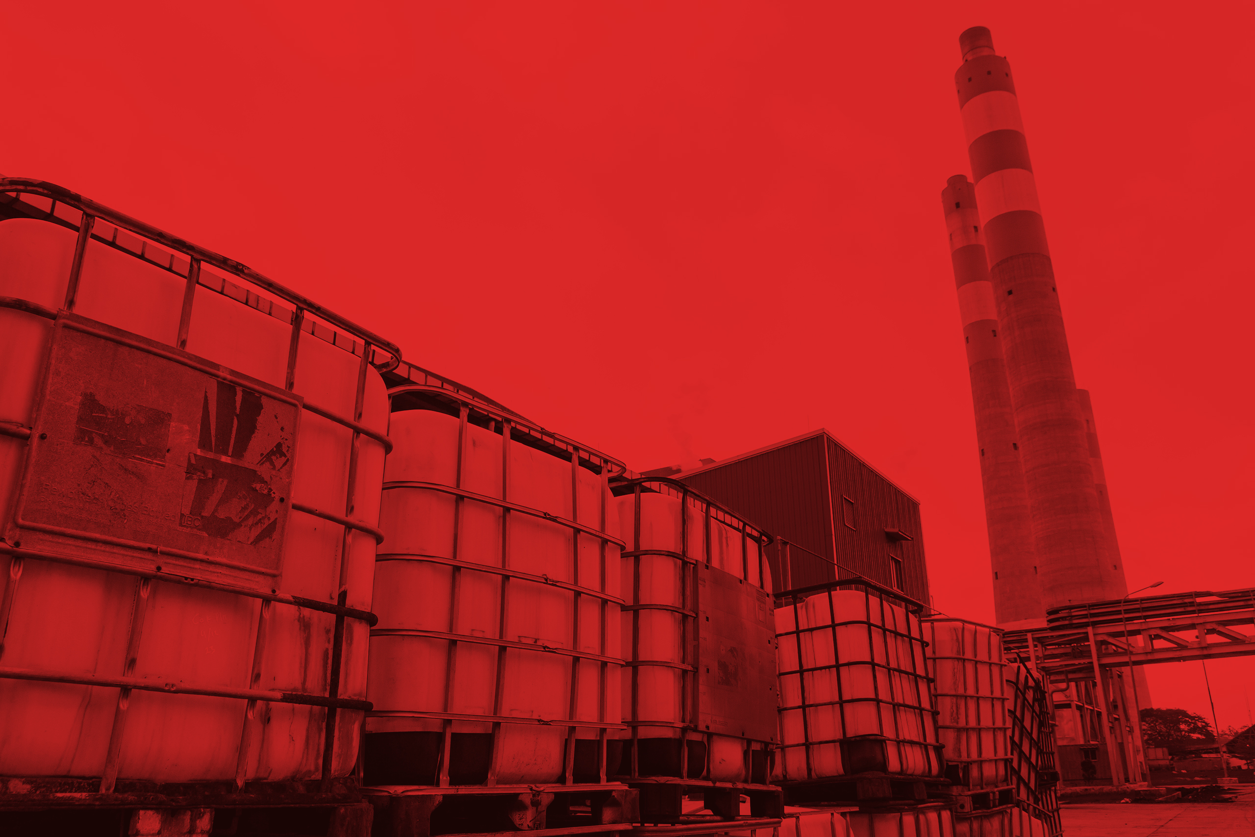 Stacked industrial containers with tall chimneys rising against a sunset sky background outside.