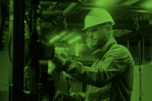 Male maintenance worker wearing safety uniform, protective glasses and hard hat check pipes using professional equipment. Engineer maintains modern commercial facility.