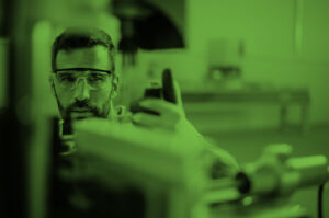 Man wearing safety glasses inspects machinery on a production line.