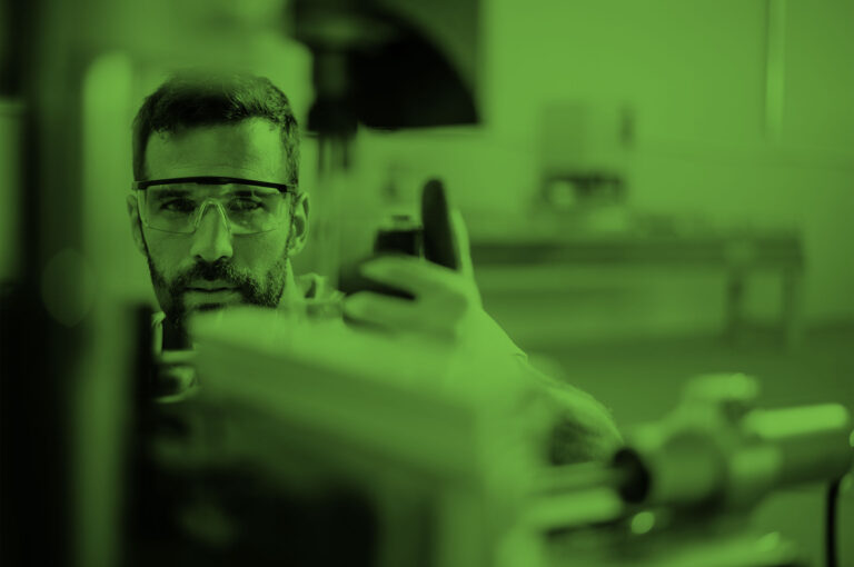Man wearing safety glasses inspects machinery on a production line.