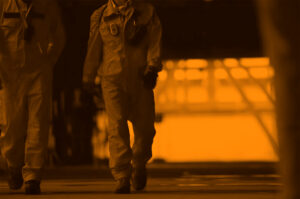 Personnel wearing safety equipment walk through a production facility.